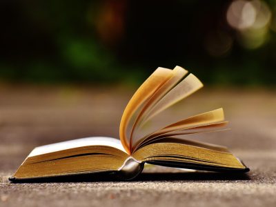 片吧内容主编老姜坐在墨绿色办公桌前翻阅资料的照片，桌面上摊开多份打印材料与一支红笔，背景书架透出暖黄灯光，呈现编辑室安静专注的工作氛围